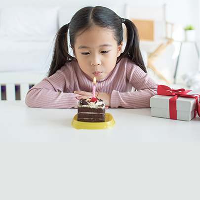 Kind sitzt vor einem Stück Kuchen und pustet die Kerze aus